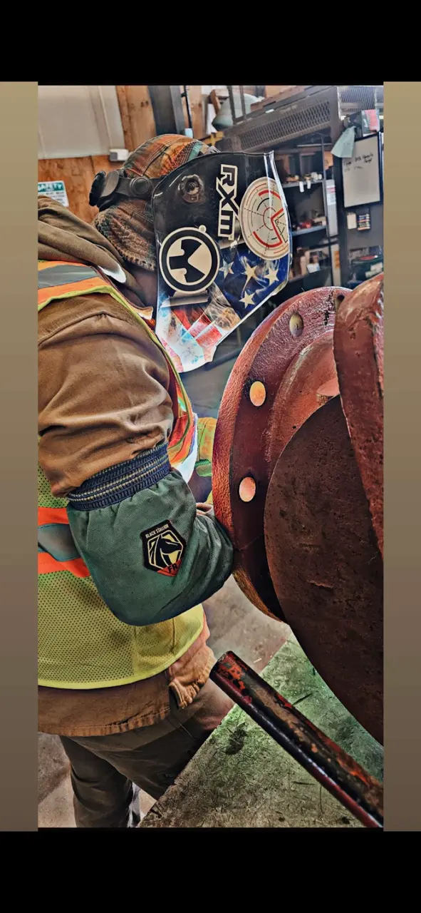 Welder with American flag helmet inspecting large steel flange