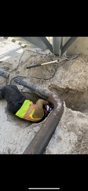 Worker welding underground pipe in excavated hole