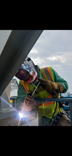 Welder in safety vest welding on structural steel beam