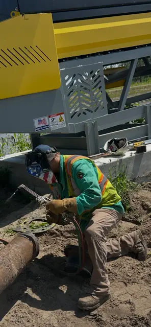 Welder cutting or welding pipe near yellow industrial equipment