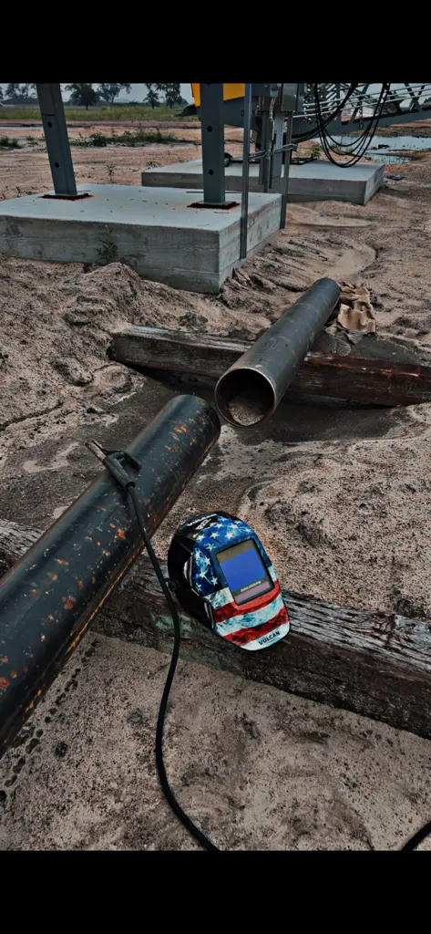 American flag welding helmet beside steel pipes on jobsite