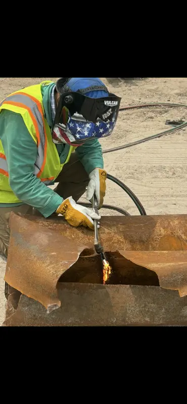 Welder torch-cutting rusty steel plate on ground