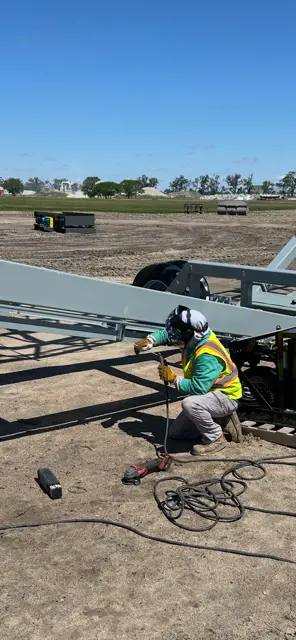 Welder kneeling welding on steel conveyor beam outdoors