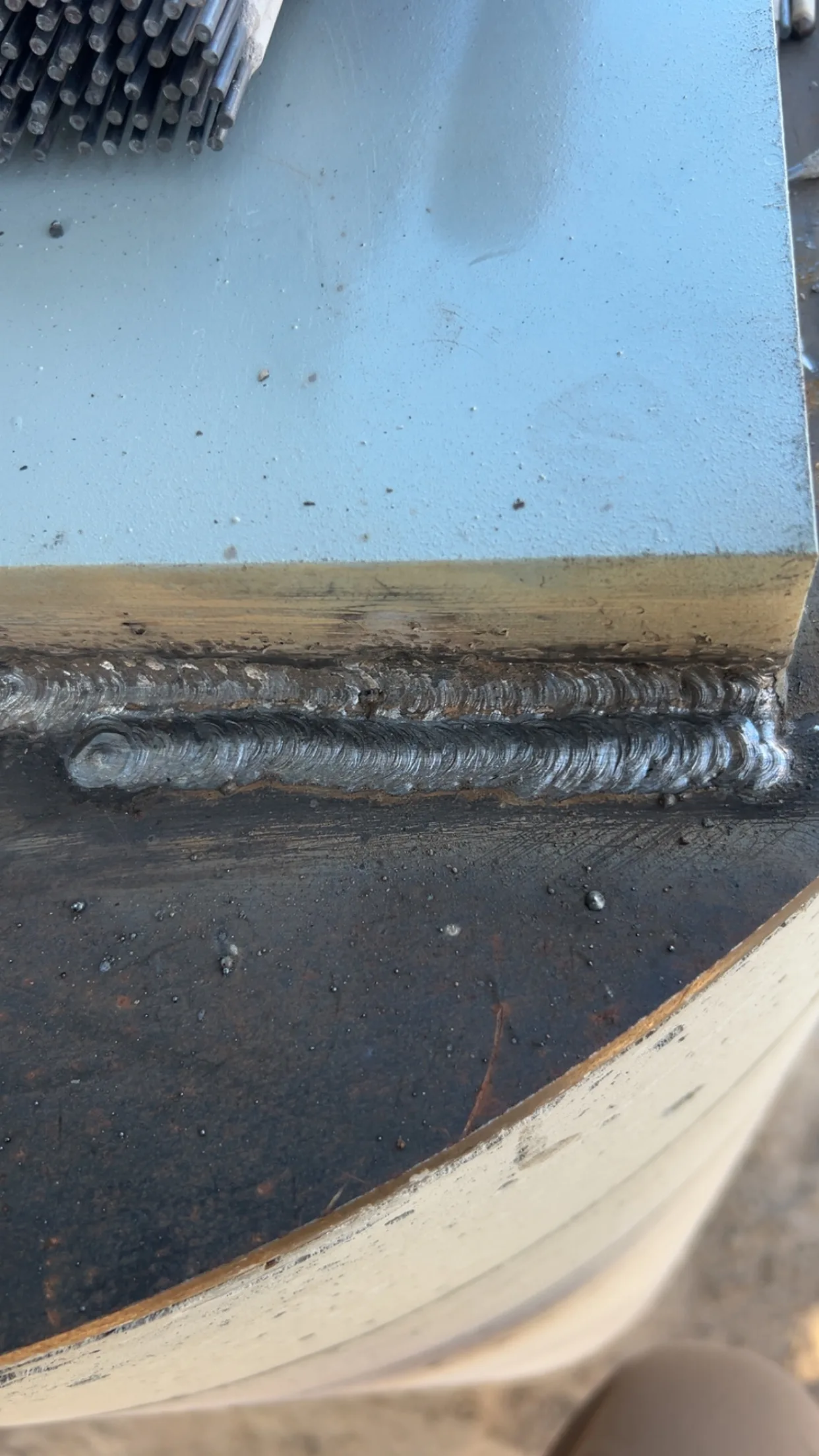 Close-up of a clean stick weld bead on plate steel with welding rods stacked nearby