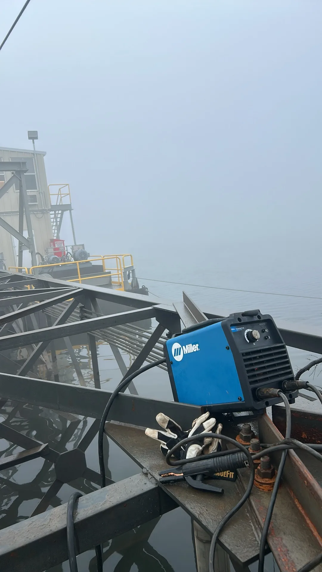 Miller stick welder set up on a foggy bridge over water with gloves and ground clamp